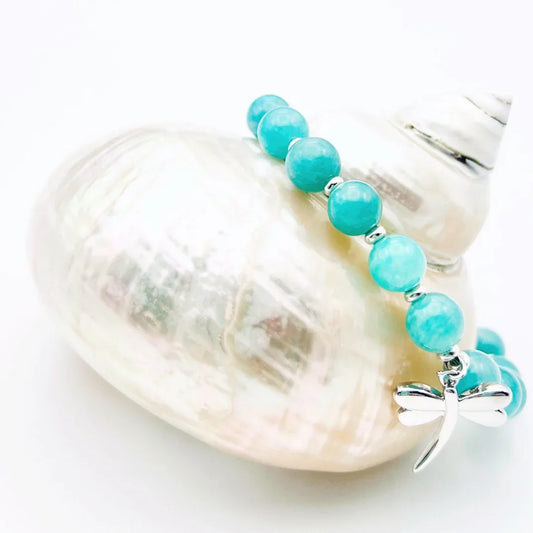 Amazonite crystal bracelet with a sterling silver dragonfly charm sitting on a shell