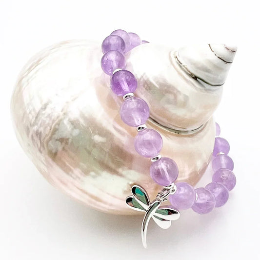 Amethyst crystal bracelet with a sterling silver dragonfly charm sitting on a shell