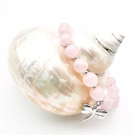 Rose Quartz crystal bracelet with a sterling silver dragonfly charm sitting on a shell