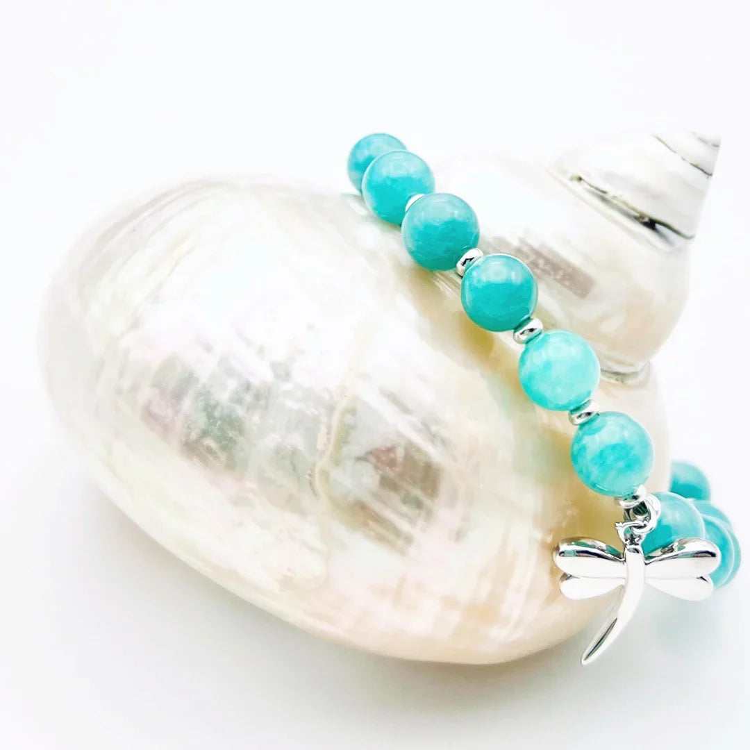 Amazonite crystal bracelet with a sterling silver dragonfly charm sitting on a shell 