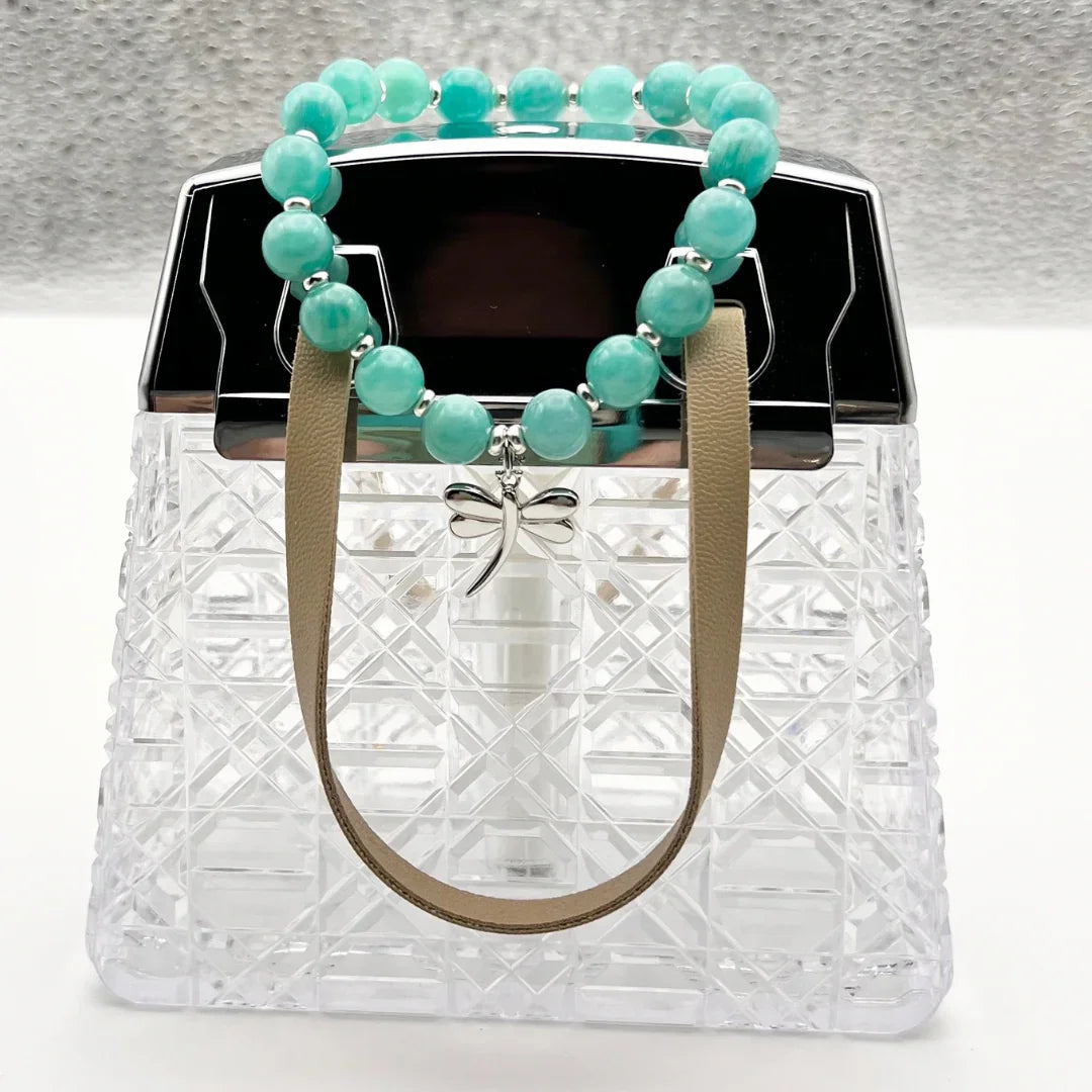 Amazonite crystal bracelet with a sterling silver dragonfly charm sitting on a clear handbag 