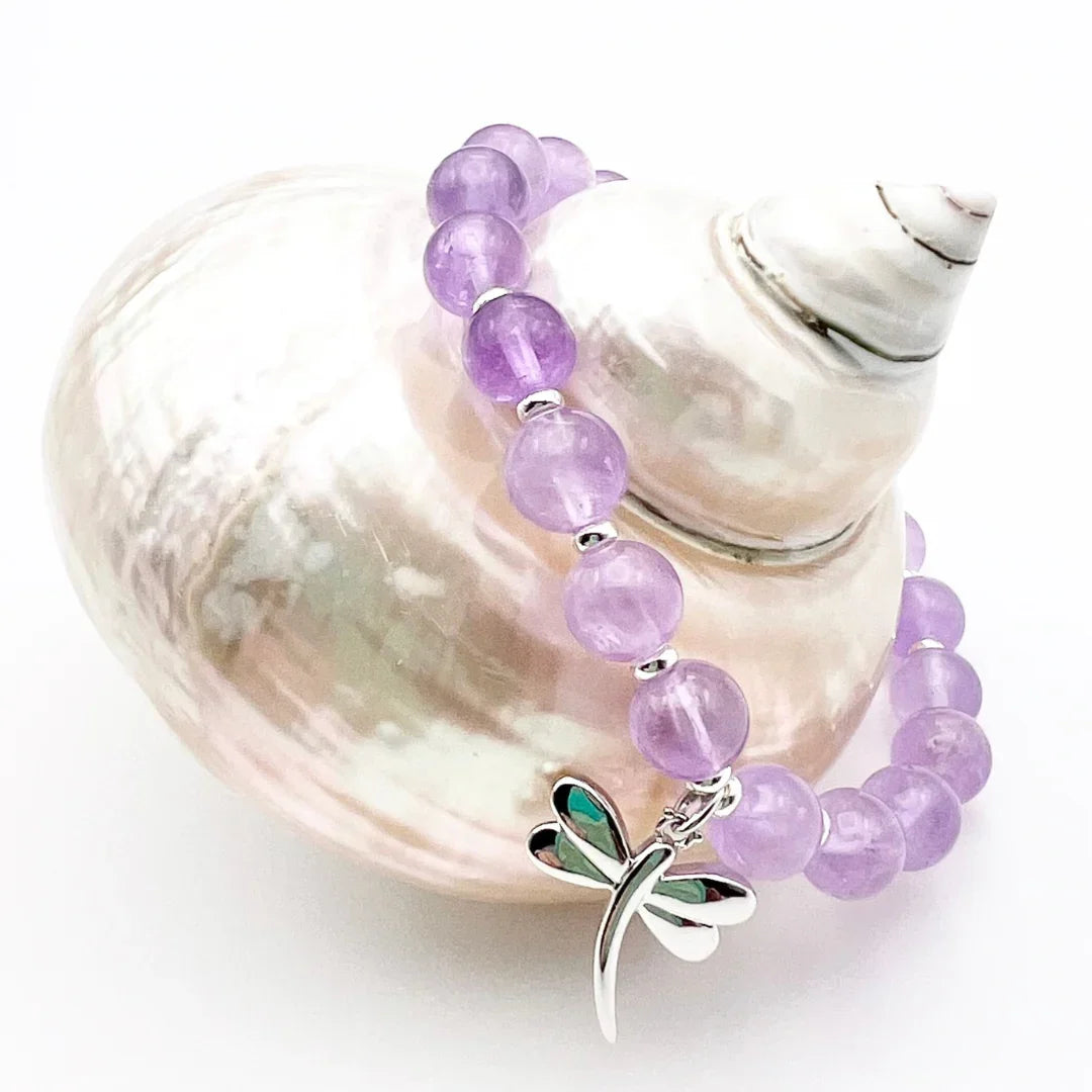 Amethyst crystal bracelet with a sterling silver dragonfly charm sitting on a shell 