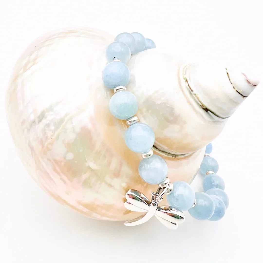 Aquamarine crystal bracelet with a sterling silver dragonfly charm sitting on a shell