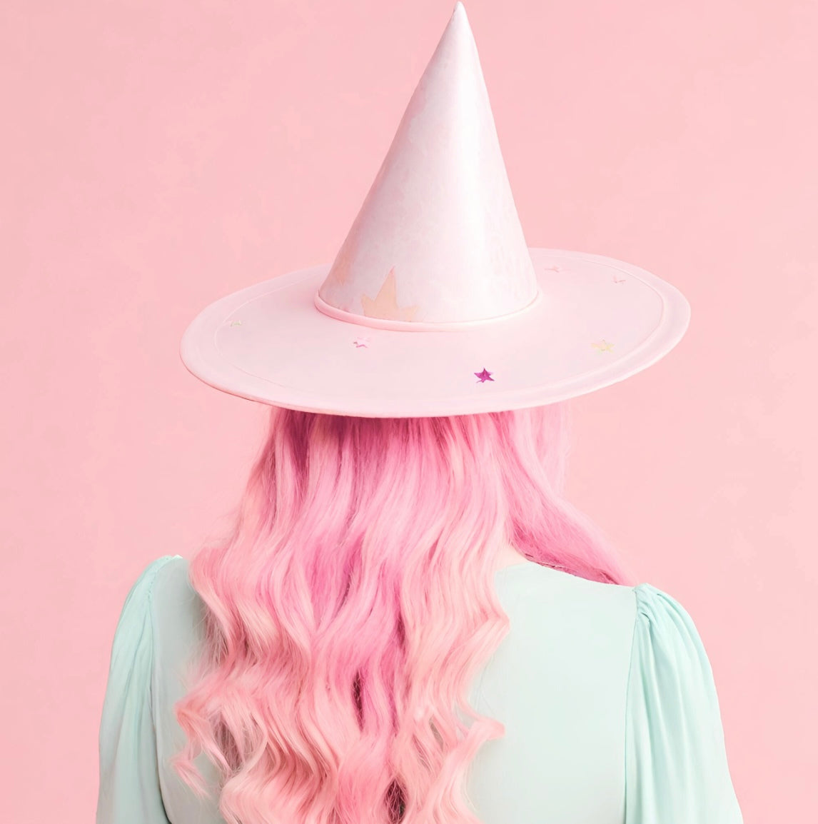 Person with pink hair wearing a pastel pink witch hat on a pink background