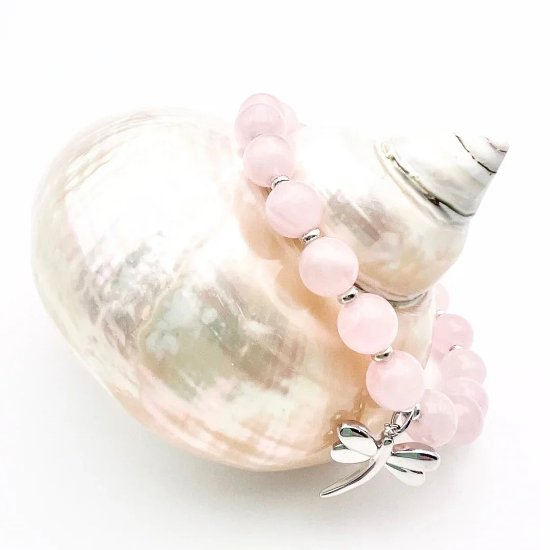Rose Quartz crystal bracelet with a sterling silver dragonfly charm sitting on a shell